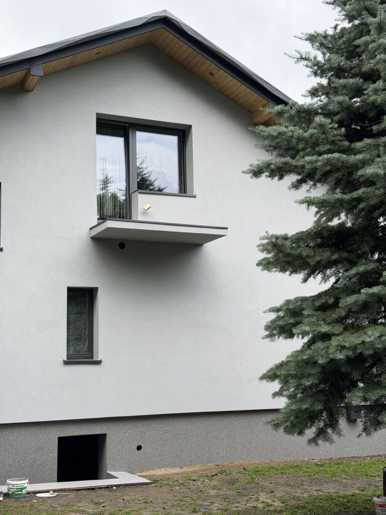 Elewacja domu jednorodzinnego z jasnym tynkiem i cokołem mozaikowym