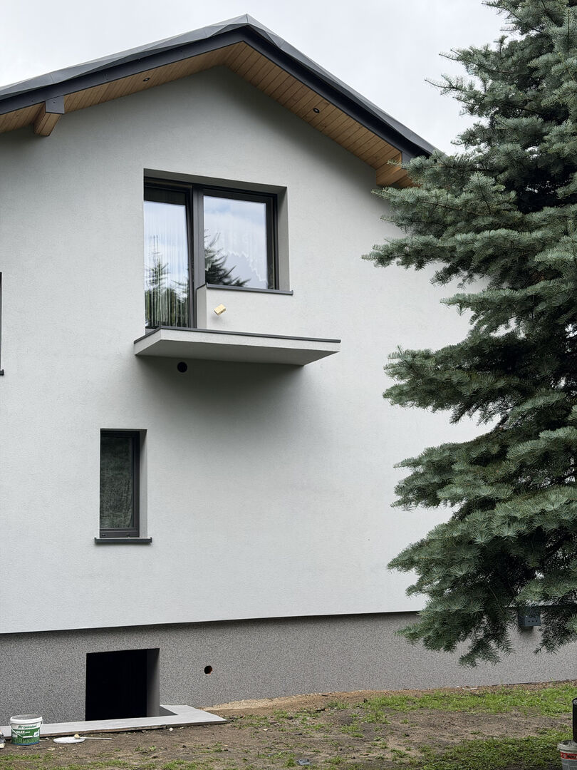Elewacja domu jednorodzinnego z jasnym tynkiem i cokołem mozaikowym